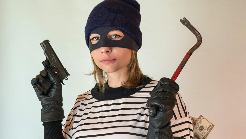 Woman posing as a thief holding a gun and crowbar with a bag of money.